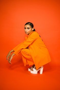 a woman in an orange outfit crouching on a white platform with her legs crossed