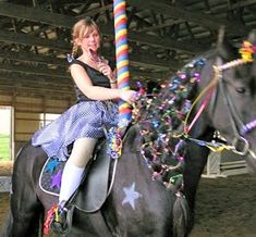 a woman riding on the back of a black horse in an indoor arena while holding onto a colorful pole