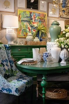 a green table topped with lots of vases and flowers next to a blue chair