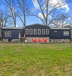 two red chairs sitting in front of a black house with trees behind it and grass on the ground