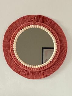 a round mirror with tassels hanging on the wall next to a white wall