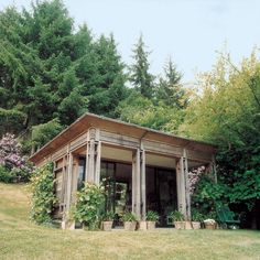 a small wooden building sitting in the middle of a lush green field next to trees