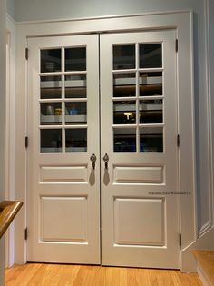 two white double doors with glass inserts on each side and wood flooring in the middle