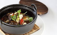 a black pot filled with food sitting on top of a white plate next to a wooden cutting board