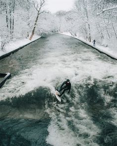 a man riding a surfboard on top of a river in the middle of winter