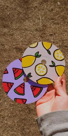 a hand holding two discs with fruit designs on them