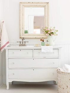 a white dresser with flowers and a mirror above it