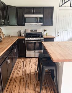 a kitchen with black cabinets and stainless steel appliances, wood counter tops and stools