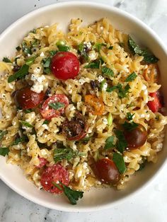 a white bowl filled with pasta, tomatoes and spinach on top of a marble table