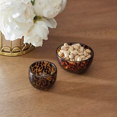 two bowls filled with nuts on top of a wooden table next to a white flower