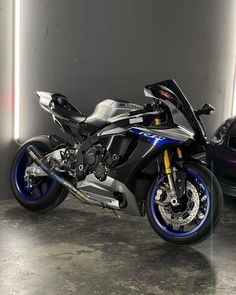 a blue and silver motorcycle parked next to a black car in a parking garage area