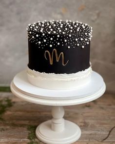 a black and white cake with gold letters on top is sitting on a pedestal in front of a wall