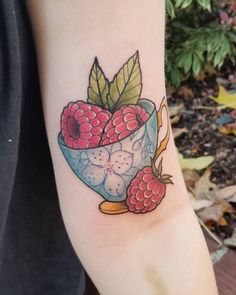 a tattoo with raspberries and leaves in a bowl on someone's arm