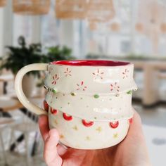 a hand holding a coffee mug with christmas decorations on the outside and red rims