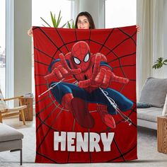 a woman holding up a red blanket with a spider man on it that says henry