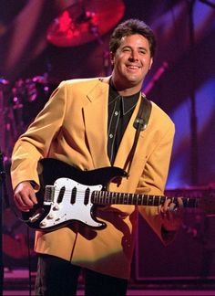 a man in a yellow suit holding a black and white guitar while standing next to a microphone