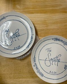 two white plates with blue lettering on them sitting on a wooden table next to each other