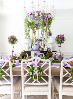 a dining room table with purple flowers and greenery on the top, surrounded by white chairs