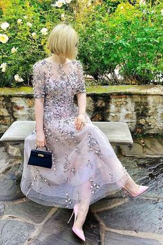 a woman is sitting on a bench wearing a dress with sequins and holding a purse