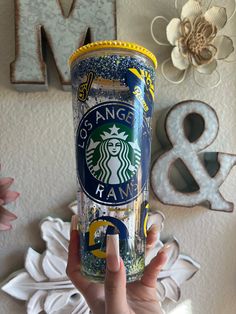 a person holding up a starbucks cup in front of a wall with letters and flowers