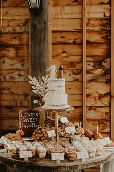 a table topped with a cake and lots of desserts next to a wooden wall