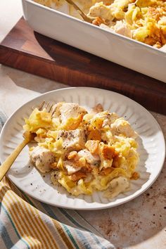 a white plate topped with pasta next to a casserole dish filled with chicken