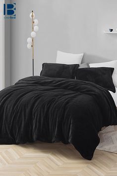 a bed with black comforter and pillows in a white room next to a window