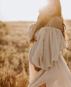 a woman in a white dress is walking through the field with her back to the camera