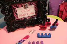 a pink table topped with different types of nail polishes and brush holders next to a framed sign that says claw painting