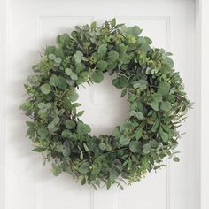 a wreath hanging on the front door of a white house with green leaves and greenery