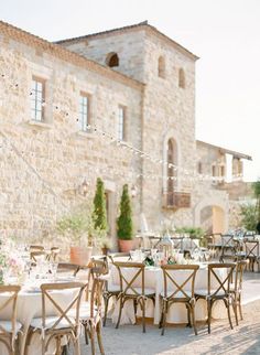 an outdoor dining area with white table cloths and wooden chairs, surrounded by stone buildings