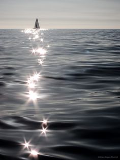 a lone sailboat in the middle of the ocean with sun shining on it's side