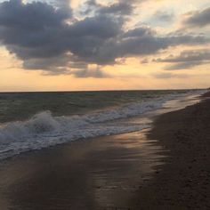 a person walking on the beach with a surfboard in their hand as the sun sets