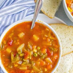 a bowl of vegetable soup next to two slices of bread on a blue and white towel