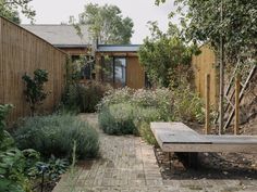 a wooden bench sitting in the middle of a garden next to a fence and building