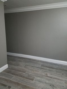 an empty room with gray walls and wood flooring in the corner is painted grey