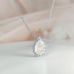 a white necklace with a tear shaped diamond in the center on a light pink background