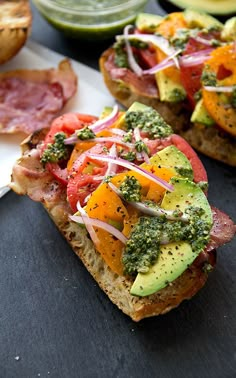 two pieces of bread with different toppings on them and avocado in the background