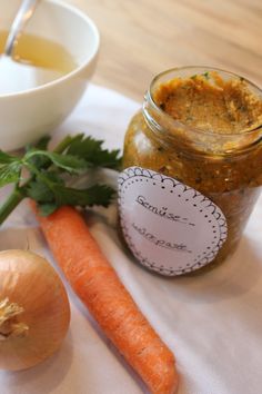 carrots and garlic on a table next to a jar of mustard with a spoon