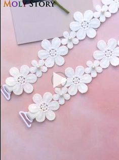 the white flowers are attached to the side of the wall hanging on the pink surface