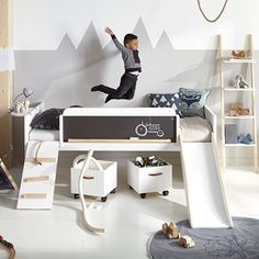 a boy jumping up into the air in his bedroom with a slide and play area