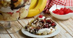 a banana split dessert on a plate with cherries and whipped cream in the background