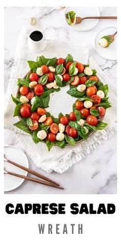 a wreath made out of tomatoes and basil leaves on top of a table with chopsticks