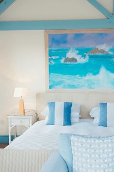 a bed with blue and white pillows in a bedroom next to a painting on the wall