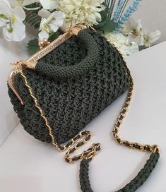 a green crocheted purse sitting on top of a white table next to flowers