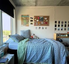 a room with a bed, desk and window in it that has pictures on the wall