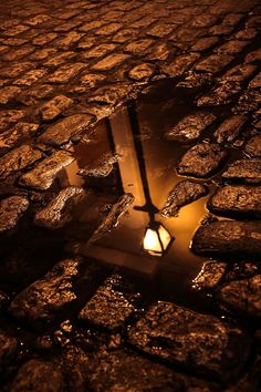 the reflection of a street light in a puddle on cobblestone pavement with spanish text