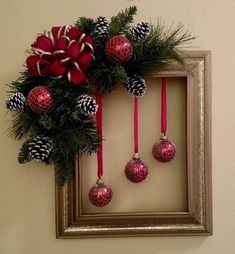 a christmas wreath with pine cones and ornaments hanging from it's side in front of a framed photo