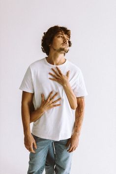 a man with his hands on his chest standing in front of a white wall and looking up