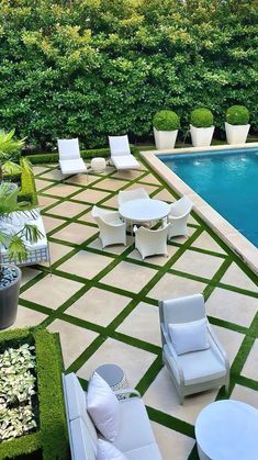 an outdoor patio with chairs and tables next to a swimming pool surrounded by greenery